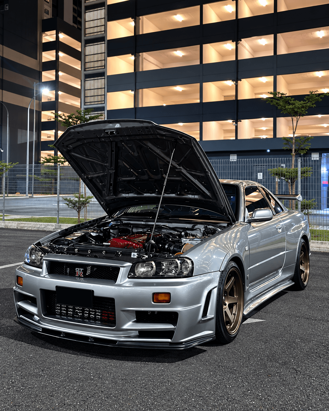 Silver Nissan Skyline GT-R R34 at night with hood raised and blank license plate